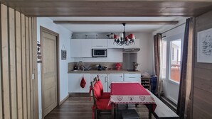 Une cuisine de taille réduite avec des meubles blancs, un four à micro-ondes et une table rouge accompagnée de chaises.