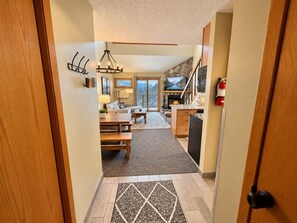 A modern kitchen with a stone fireplace, a dining area with a wooden table and benches, and a view of a mountainous landscape through large windows. - Lutsen Ski-In/Ski-Out | Moose Mtn Views | Hot Tub (Lutsen)