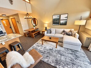 A modern living room with a sofa, coffee table, and a dining area with a table and chairs. - Lutsen Ski-In/Ski-Out | Moose Mtn Views | Hot Tub (Lutsen)