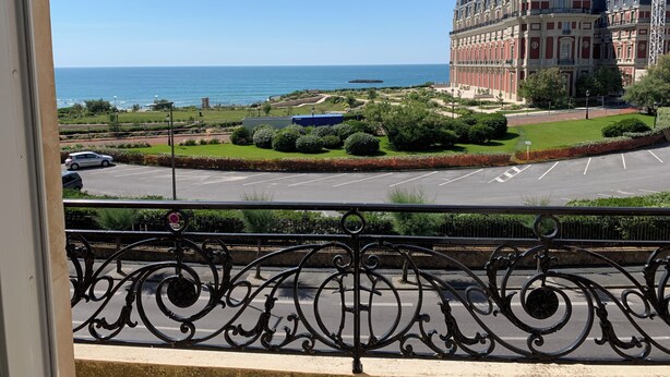 A view from a balcony overlooking a coastal area with a large building, a parking lot, and a clear blue sky. - Apt. Biarritz Rés Carlton, Grande plage (Biarritz)