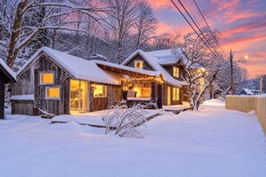 A wooden cabin with a snow-covered roof, a porch with string lights, and a visible window. - Scenic Rt 4: Hot tub, minutes to everything! (Bridgewater)