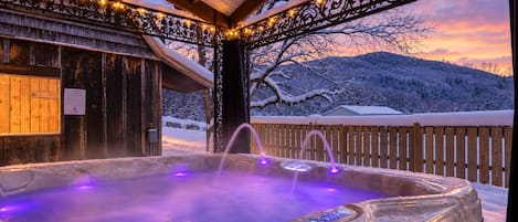 Un jacuzzi con cubierta de madera y vistas a colinas nevadas.