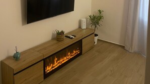 Una sala de estar moderna con un televisor de pantalla plana montado en la pared, una mesa consola de madera con chimenea integrada y una planta en maceta.