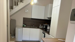 Una cocina compacta con armarios blancos, una encimera de madera y una lámpara colgante.