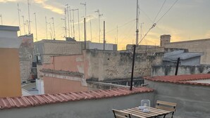 Una terraza en la azotea con una mesa y sillas, piso de baldosas y vistas de edificios y líneas eléctricas circundantes.