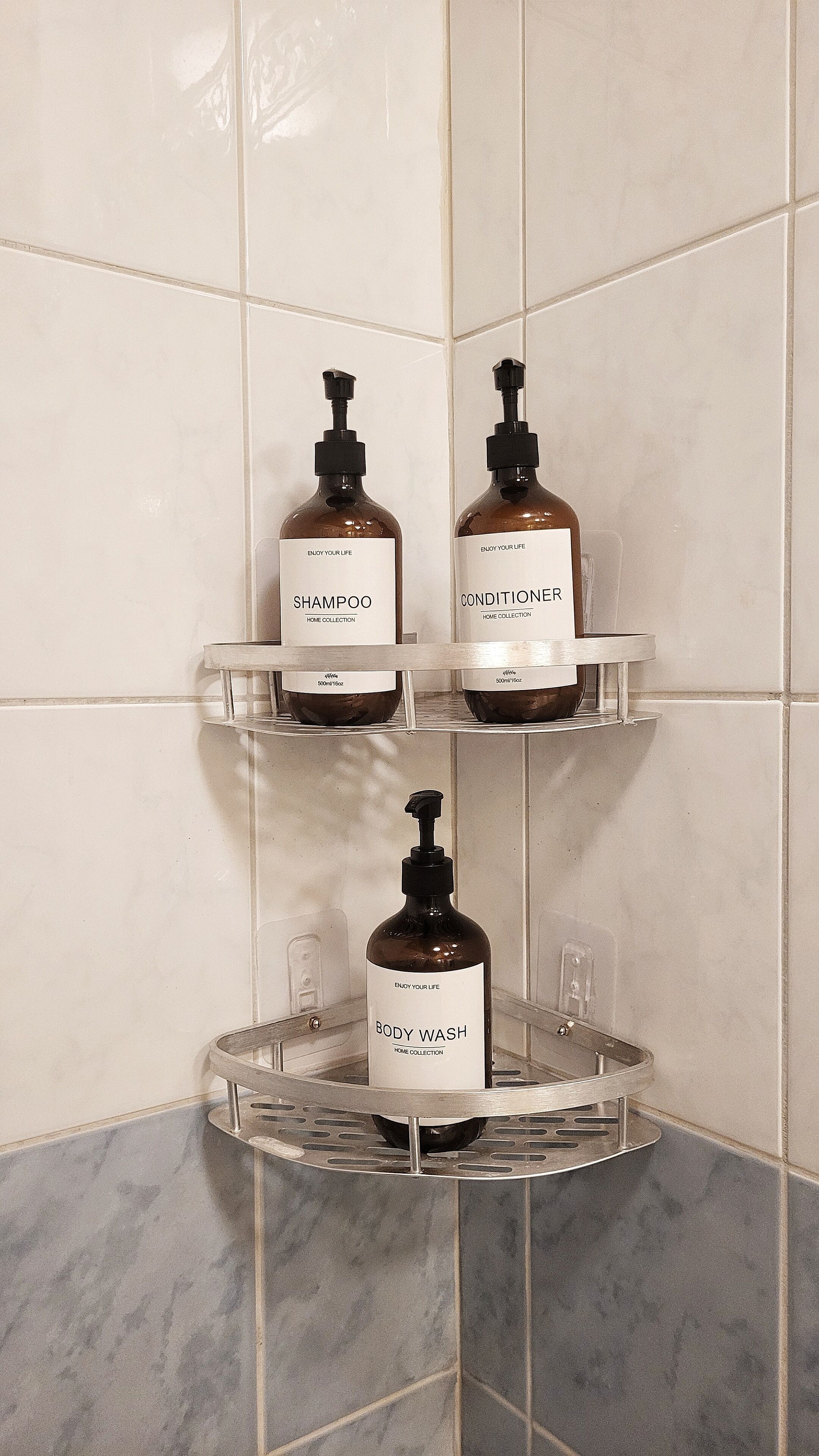 Une étagère de salle de bain avec trois flacons de produits de toilette : du shampooing, de l’après-shampooing et du gel douche.