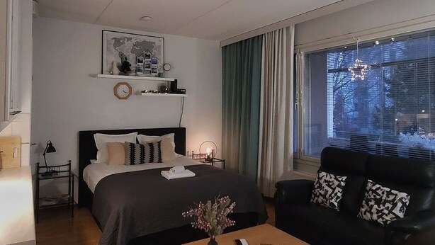 A modern hotel room with a bed, a sofa, a coffee table, and a window with curtains. - Lakeside Serenity in Lutakko | sauna, parking, A/C (Jyväskylä)