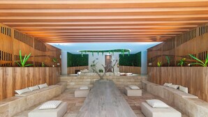 Un espacio interior moderno con un largo banco de madera, asientos acolchados y un arreglo floral central.