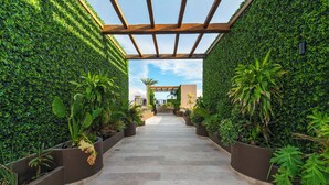 Un sendero bordeado por muros verdes y jardineras, que conduce a la entrada de un edificio.