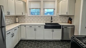 Een moderne keuken met witte kastjes, een zwart aanrecht, een vloer van honingraatmozaïek en een raam met zonwering.