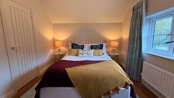 A bedroom with a bed, two bedside tables, a window with curtains, and a radiator.
