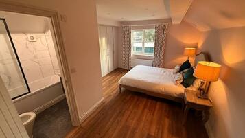 Un dormitorio con cama, mesita de noche con lámpara, ventana con cortinas y vistas al exterior.