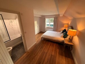 A bedroom with a bed, a nightstand with a lamp, a window with curtains, and a view of the outside.