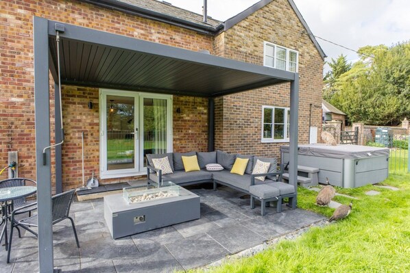 A covered patio with a grey sofa, outdoor table, and chairs.