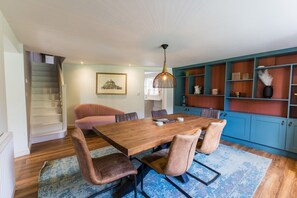 A dining area with a wooden table and chairs, a staircase, and a bookshelf with various items.