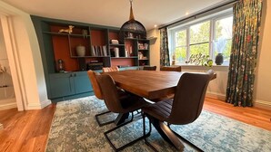 Un coin repas avec une table et des chaises en bois, une bibliothèque et une fenêtre avec des rideaux.