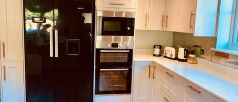 A modern kitchen with white cabinetry, a black refrigerator, a built-in oven, and a countertop with a toaster and other appliances.