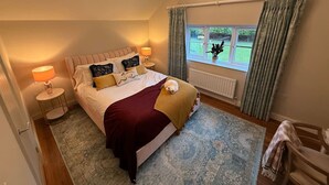 Une chambre avec un grand lit, une lampe de chevet, une fenêtre avec des rideaux et une vue sur l’extérieur.