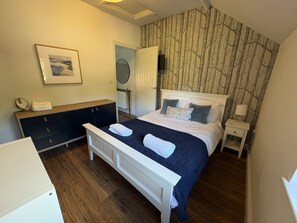 A bedroom with a bed, bedside tables, a dresser, a mirror, and a wall-mounted TV.