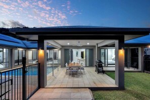 Una casa moderna con patio coperto, piscina e zona barbecue.
