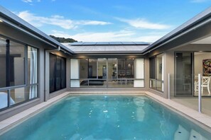 Una piscina interna moderna con pareti in vetro, tetto piatto e un’area relax visibile.