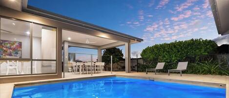 A modern house with a swimming pool, a covered patio, and a view of the sky.