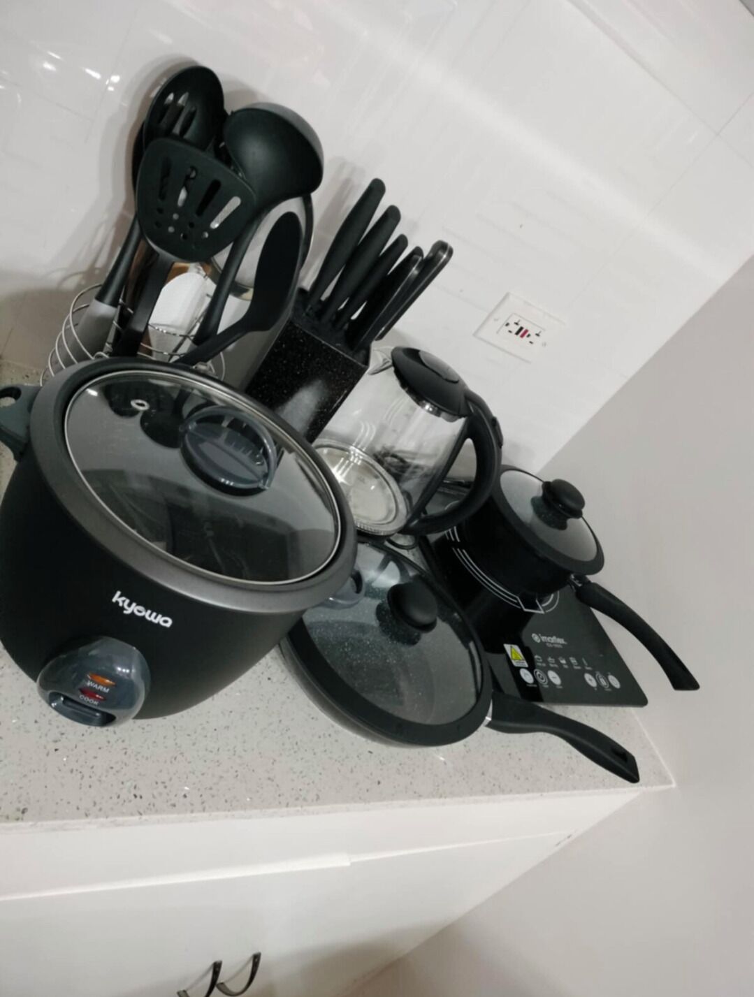A kitchen with a black Kyowa rice cooker, a glass container, and various utensils.