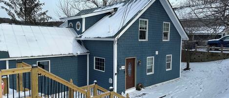 A two-story house with a blue exterior, a wooden staircase, and a metal roof.