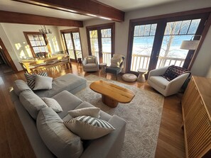 A spacious living area with a sofa, armchairs, a coffee table, and a view of a balcony. - Charming Lakefront Cottage on Lake Mascoma (Enfield)