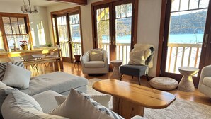 Amplia sala de estar con un sofá grande, dos sillones, una mesa de centro de madera y vista a un lago a través de amplias ventanas.