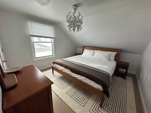 Une chambre à coucher comprenant un lit, une table de chevet, une fenêtre avec des stores, un luminaire au plafond et un tapis à motifs.