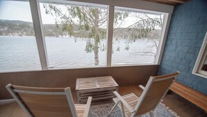 Una habitación con un gran ventanal que da a un paisaje nevado, dos sillas de madera y una pequeña mesa.
