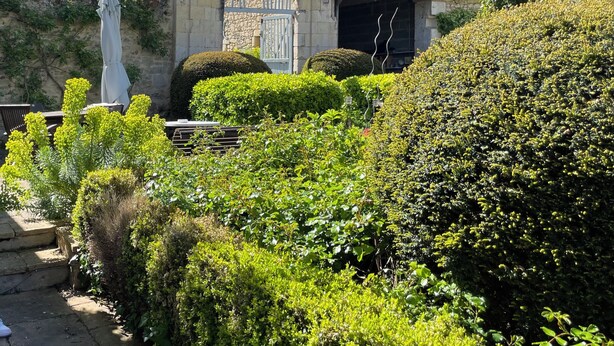 Ein Garten mit einem Steinhaus, einer Statue und gepflegten Hecken.