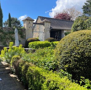 Un jardin agrémenté d’un bâtiment en pierre, d’une statue et de haies bien entretenues.