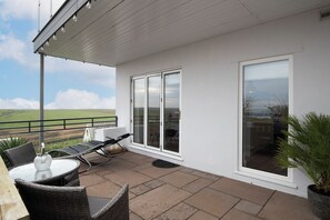 A covered patio with a table and chairs, a large sliding glass door, and a view of the landscape. - Blue Horizon - Spectacular Coastal Views (Penally)