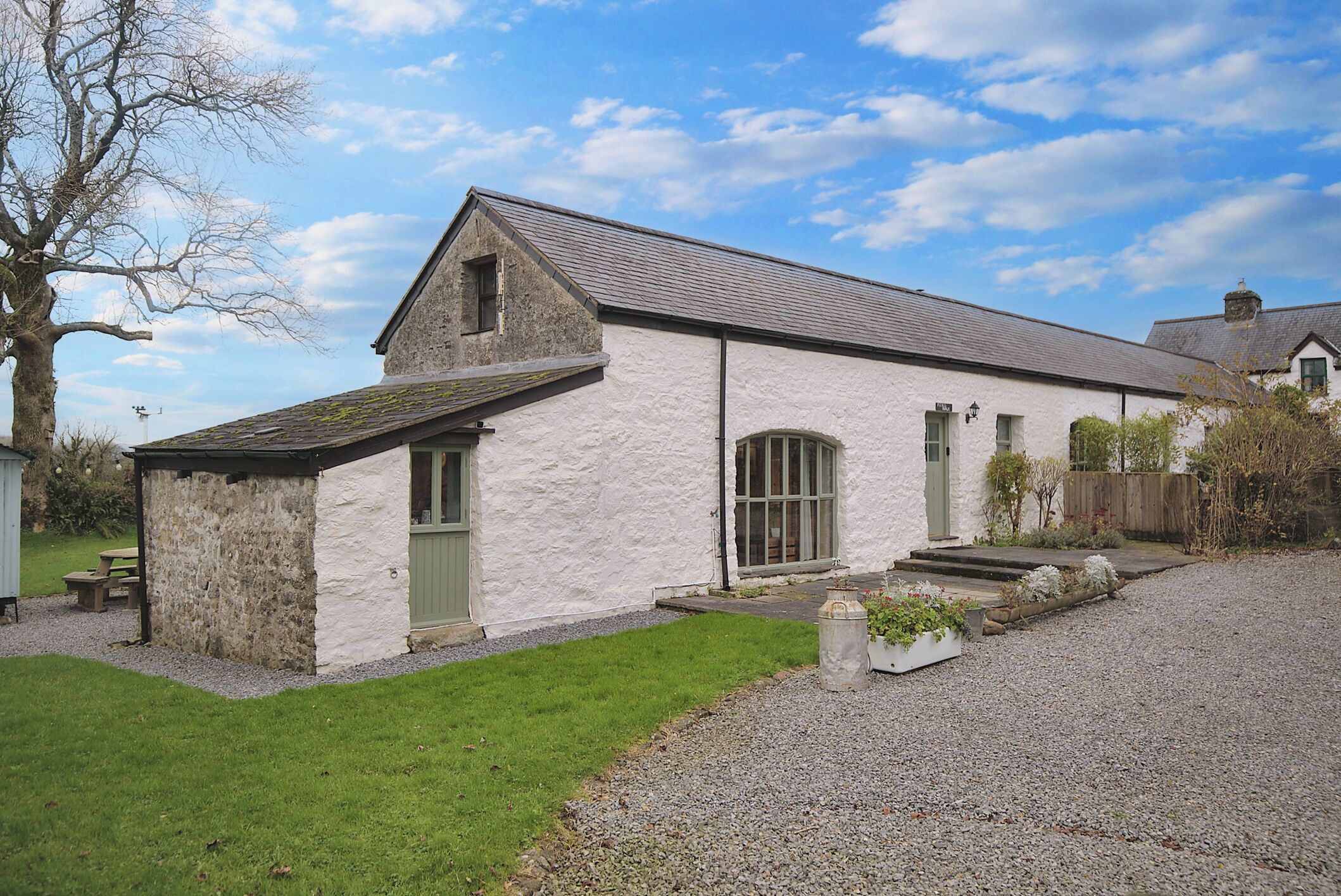 A white building with a stone foundation, a pitched roof, and a gravel driveway.