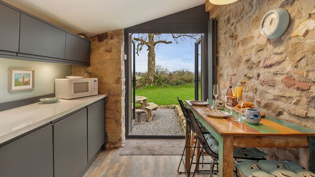 A modern kitchen with a stone wall, a wooden dining table, and a view of a garden.