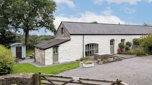 A white stone building with a gravel driveway, a wooden gate, and a small shed.