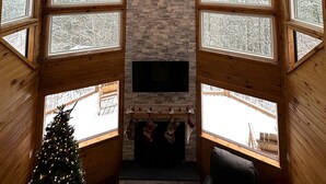 Een gezellig interieur van een blokhut met een stenen openhaard, een bevestigde televisie en een bijzondere hanglamp van gewei.