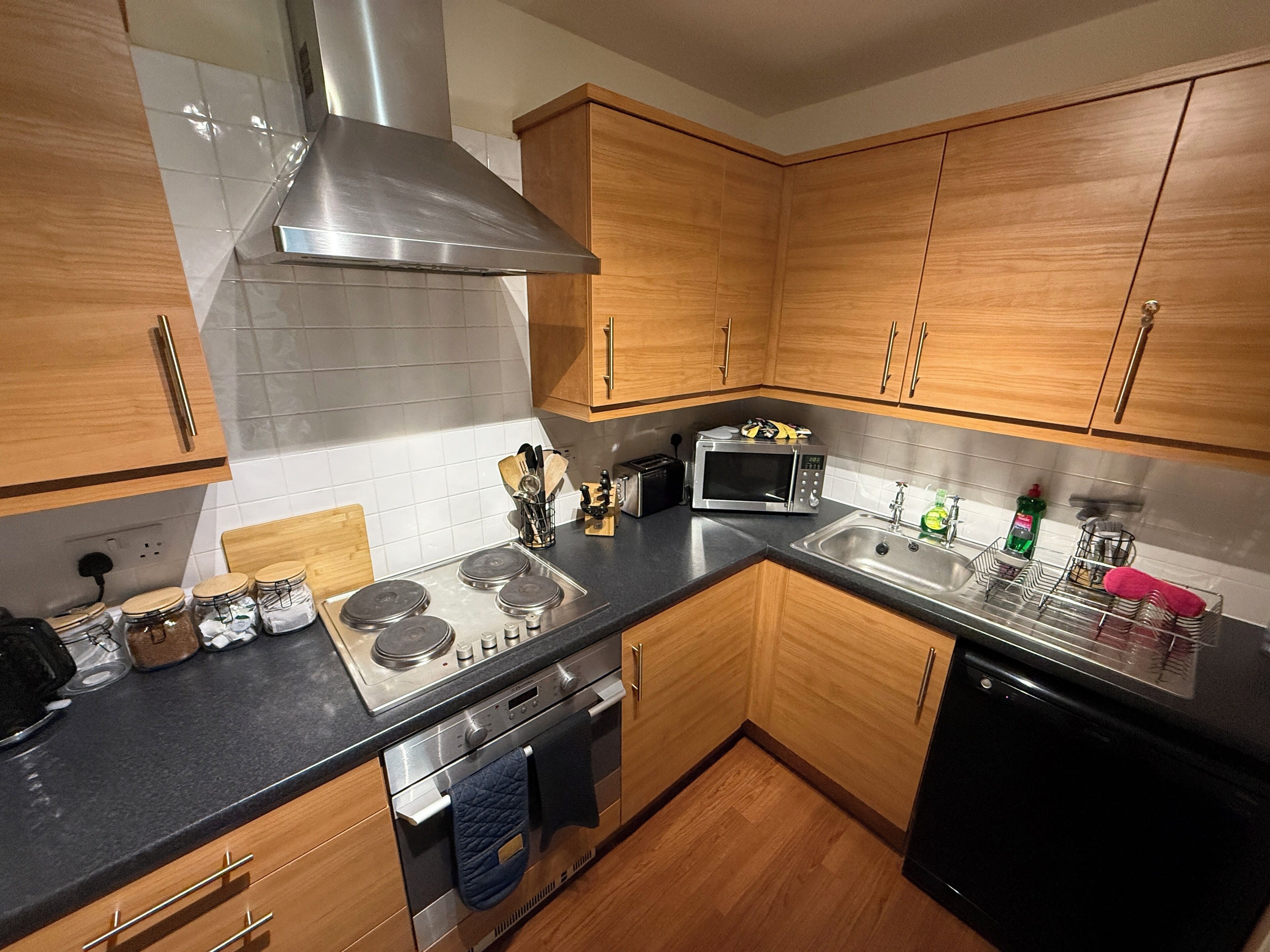 A modern kitchen with wooden cabinets, a stainless steel range hood, a microwave, a toaster, and a dishwasher.