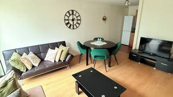 A modern living room with a sofa, a coffee table, a dining table with chairs, a TV, and a clock on the wall.