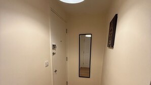 Un pasillo estrecho con suelo de madera, una puerta al final y una lámpara colgante.