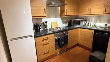 A modern kitchen with wooden cabinets, a white refrigerator, a microwave, and a dishwasher.