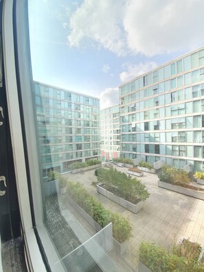 Un edificio moderno con varios pisos y grandes ventanales. Cuenta con un patio con macetas y zonas de estar.