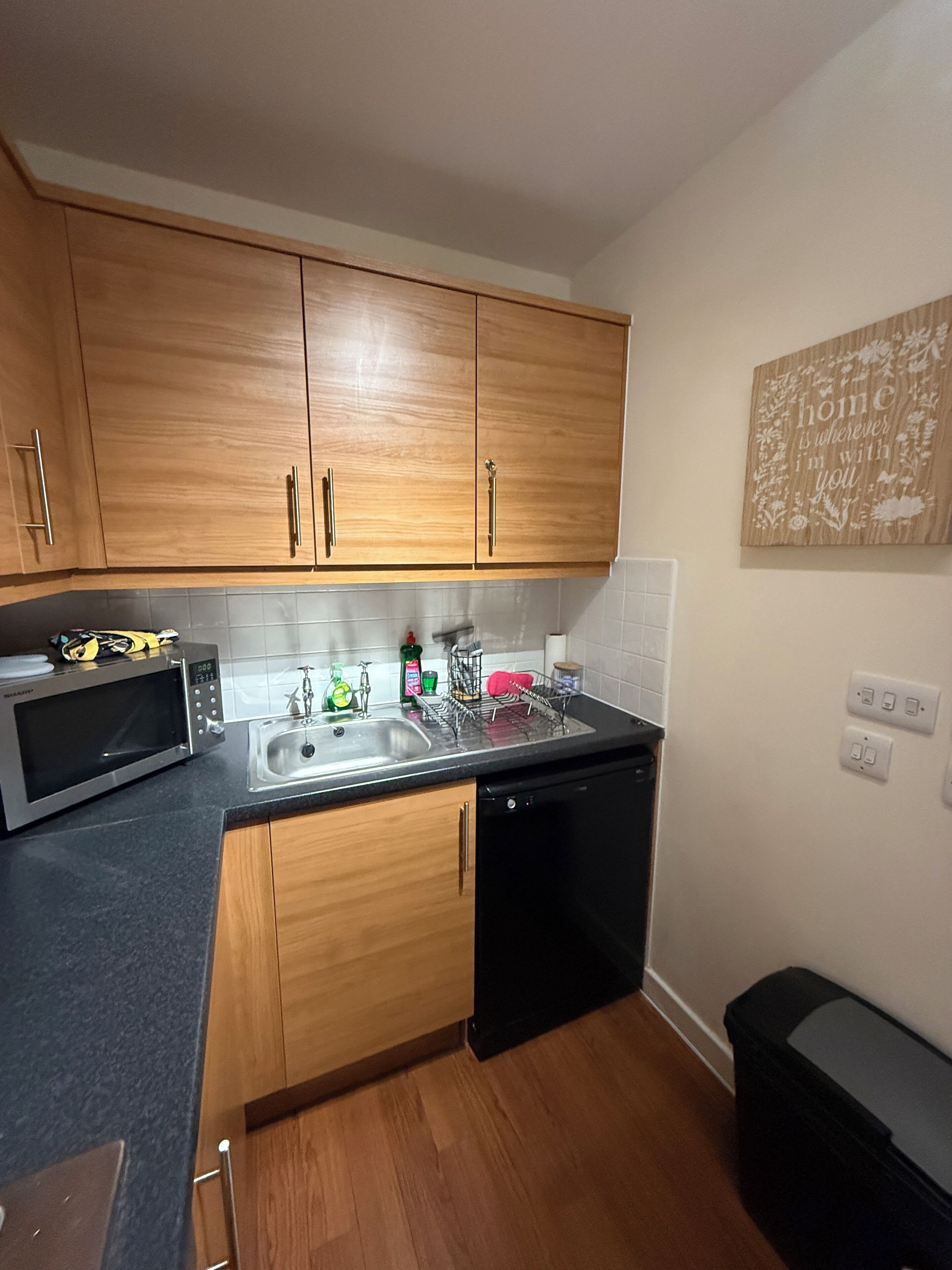 A compact kitchen with wooden cabinets, a microwave, a sink, and a dishwasher.