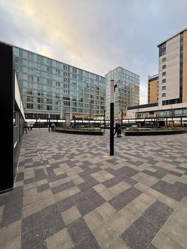 A plaza with a checkered floor pattern, modern buildings, and a clear sky.