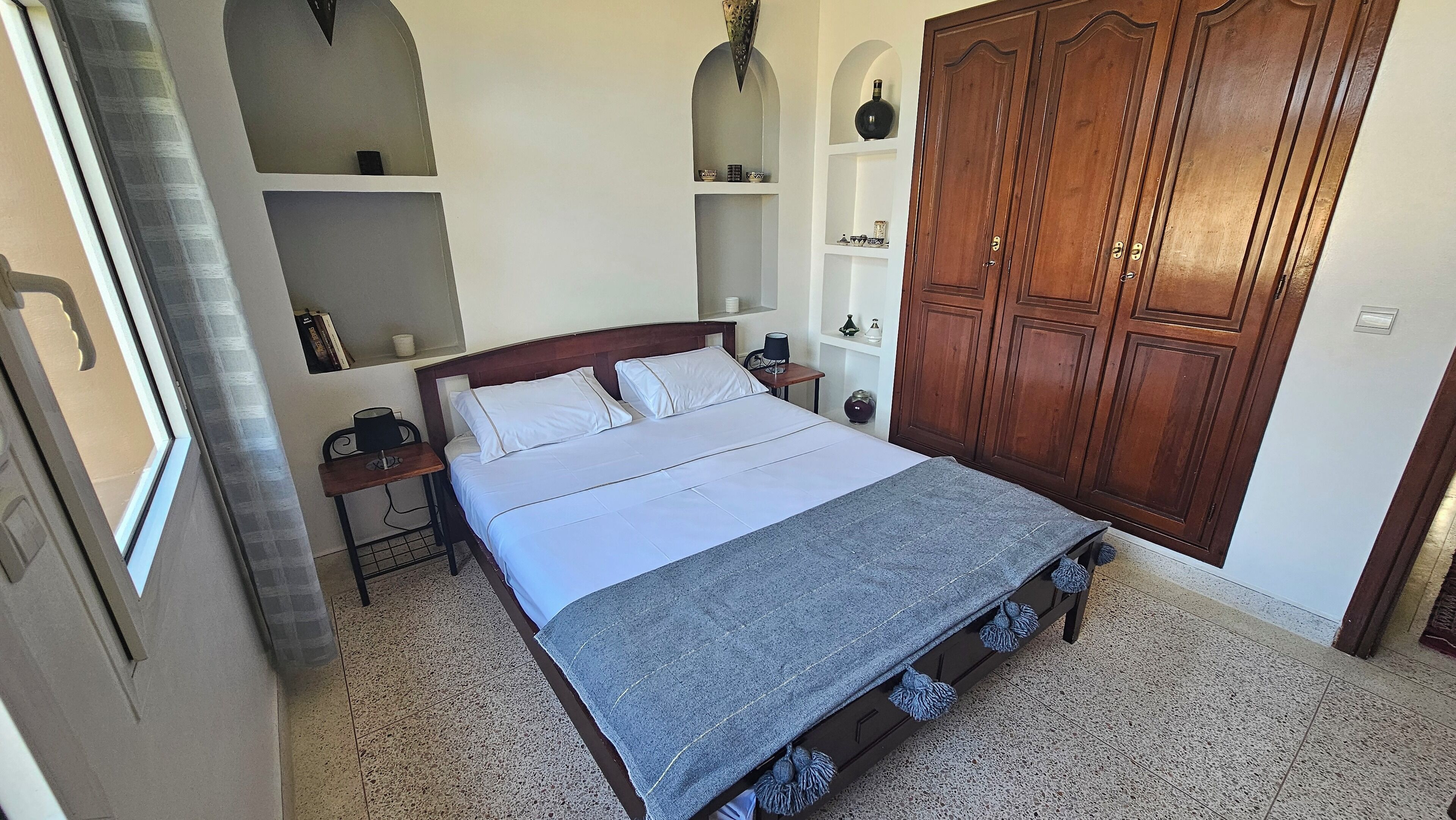 Une chambre à coucher bien rangée, avec un lit, des tables de chevet, une armoire et des étagères intégrées.