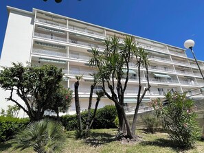 Un hôtel à plusieurs étages doté de balcons, entouré de plantes tropicales et surplombant un ciel d’un bleu limpide.