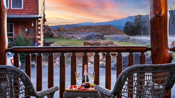 A wooden deck with wicker chairs and a table set with a bottle, glasses, and snacks. - Indoor Pool Cabin, Hot Tub & Theater Room, Near Dollywood, Game Room, Sleeps 14 (Pigeon Forge)