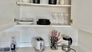 Una cocina con armarios blancos, un tostador, una cafetera y distintos platos y utensilios.